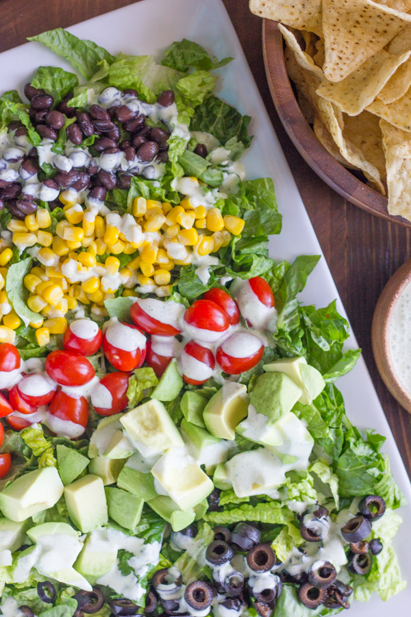 Healthy Chopped Taco Salad on a serving platter, with a bowl of tortilla chips and a small bowl of creamy cilantro lime dressing next to the platter.  