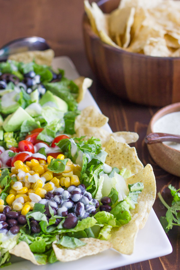 Healthy Chopped Taco Salad on a serving platter with some tortilla chips, with a small bowl of creamy cilantro lime dressing and a bowl of tortilla chips next to the platter.  