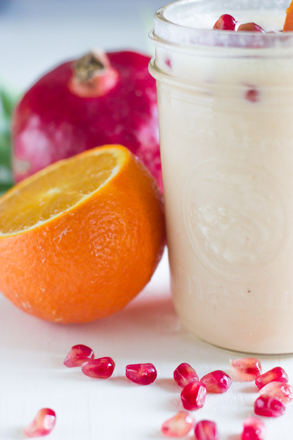 Pomegranate Citrus Smoothie in a glass jar with pomegranate seeds on top, with an orange and pomegranate next to the glass.  