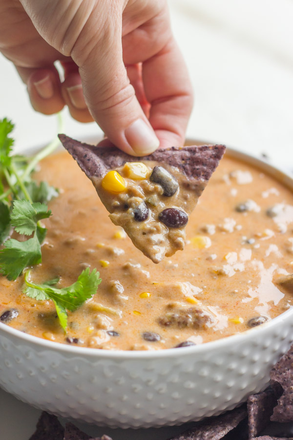 Homemade Chili Queso in a bowl with a tortilla chip that has been dipped in the queso. 