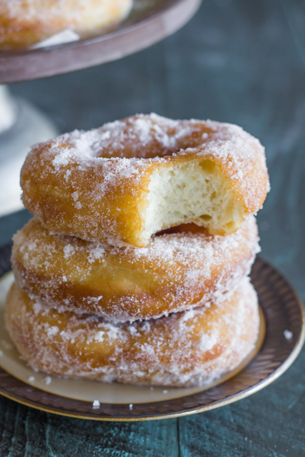 Homemade Yeast Doughnuts stacked in a pile of three on a plate, with a bite taken out of the top donut.  