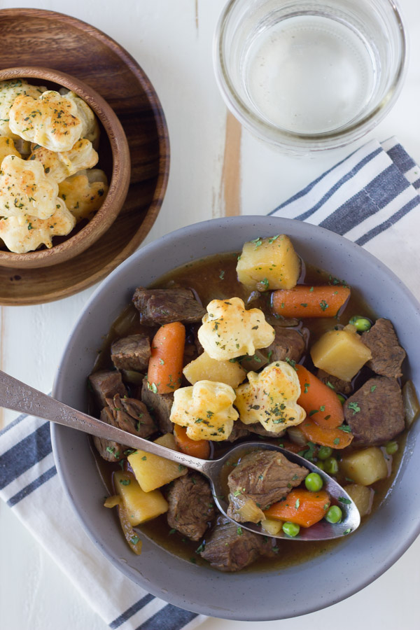 Irish Beef Stew in a bowl with a spoon and a wood bowl of Shamrock Croutons next to it, along with a glass of water.  