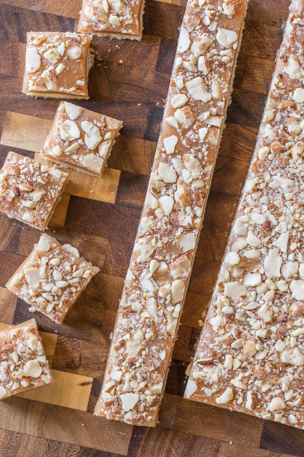 Homemade Caramel Almond Shortbread Bites being cut into squares on a cutting board. 