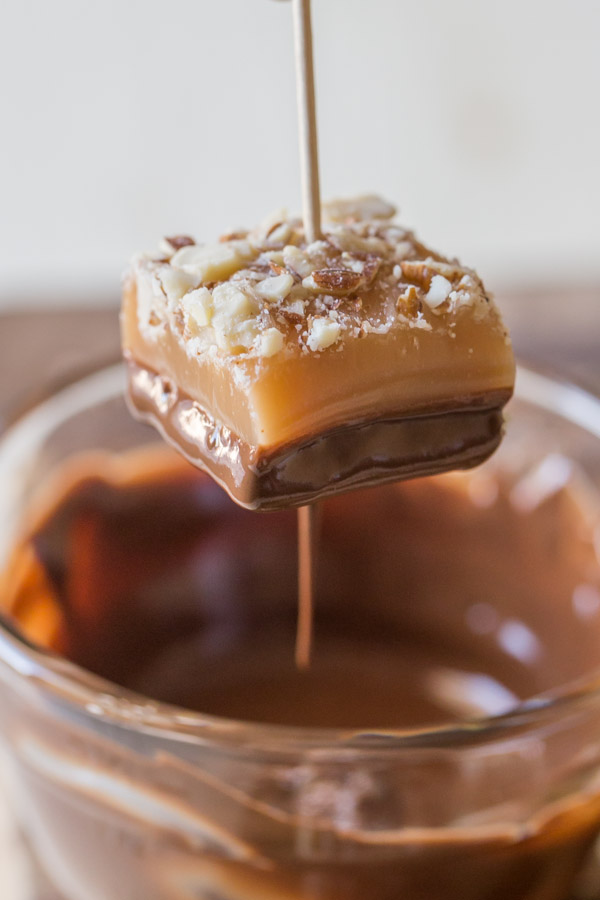 Homemade Caramel Almond Shortbread Bite with a toothpick in it, that has just been dipped into the melted chocolate.  