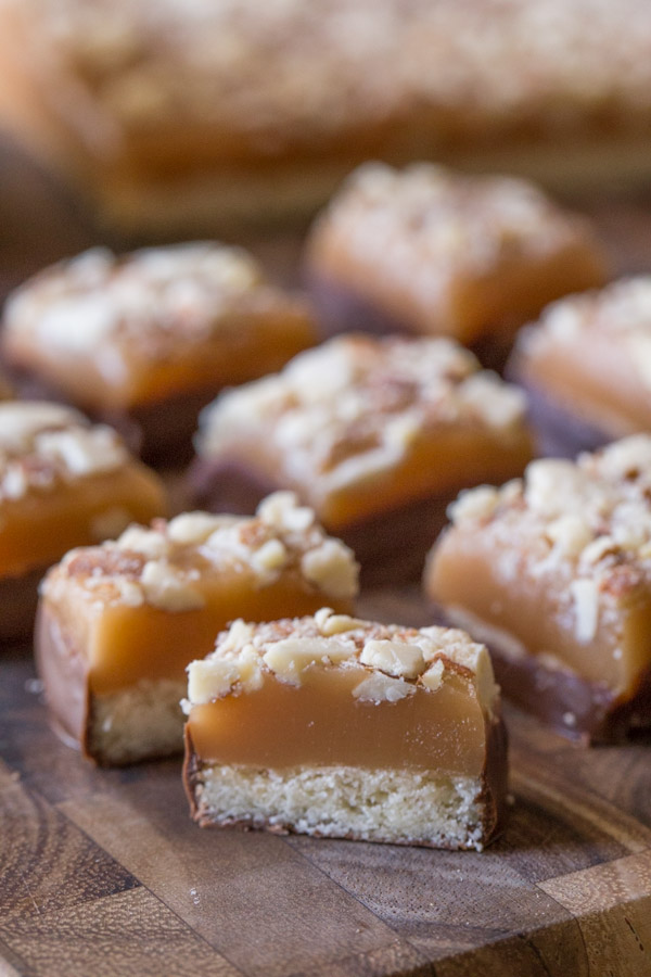 Homemade Caramel Almond Shortbread Bite cut in half, sitting on a cutting board with more Homemade Caramel Almond Shortbread Bites.