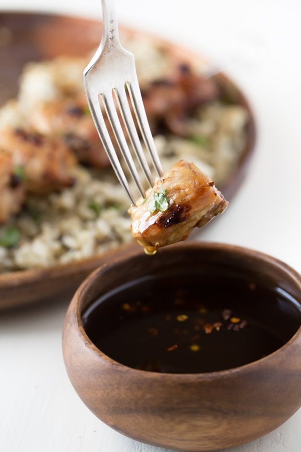 A piece of Maple Dijon Glazed Chicken on a fork that has been dipped into a small bowl of the Maple Dijon Glaze.  
