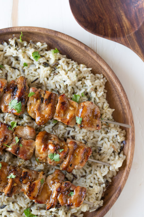 Maple Dijon Glazed Chicken served over a bed of rice on a wood plate.  