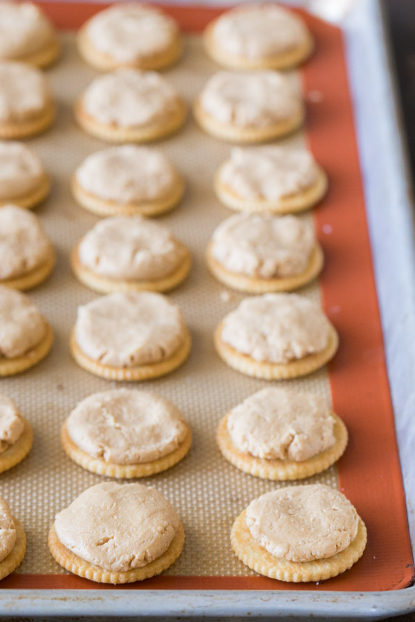 Ritz crackers arranged on a Silpat lined baking sheet, with a scoop of the peanut butter filling slightly flattened on top of each cracker.  