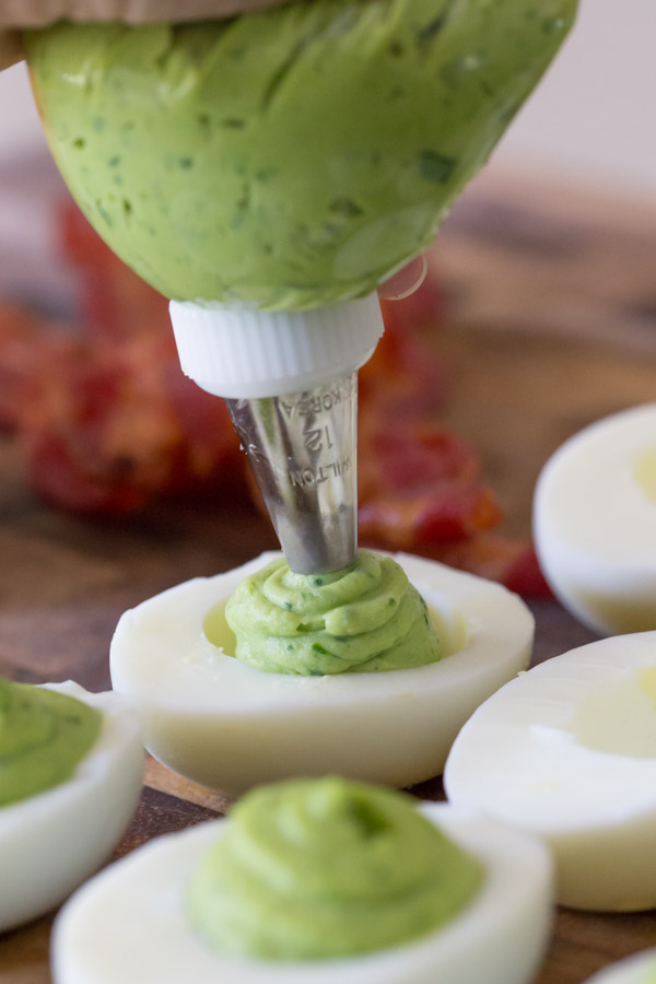 A bag with a tip being used to pipe the filling into the egg white halves for the Smoky Bacon Avocado Deviled Eggs.