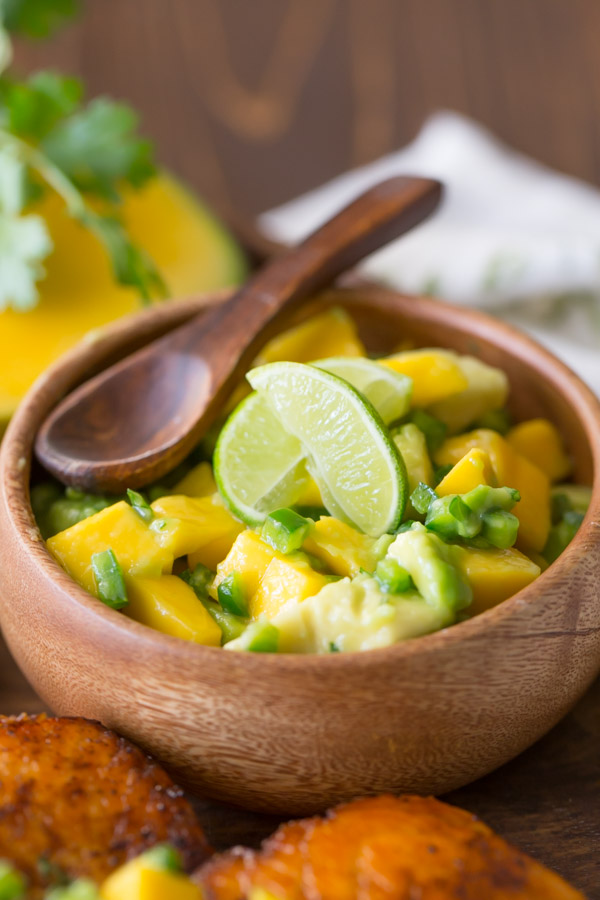 A small wood bowl of Mango Avocado Salsa with a small wood spoon in it. 