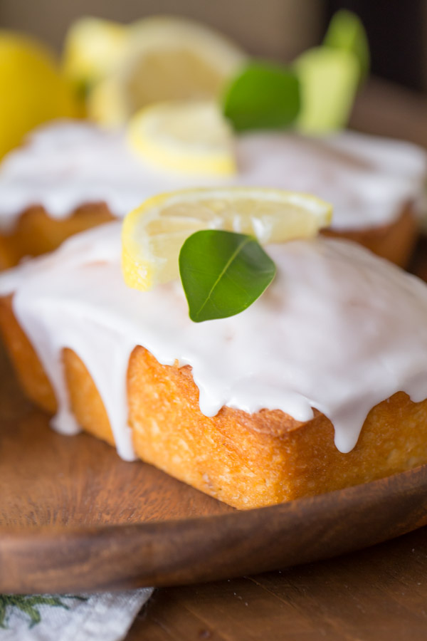 Mini Iced Lemon Pound Cake Loaves garnished with a lemon wedge and green leaf on a wood serving tray. 