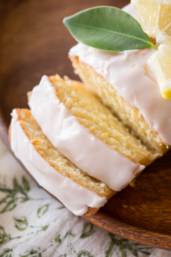 Mini Iced Lemon Pound Cake Loaf garnished with a lemon wedge and green leaf, that has two slices ready for serving. 