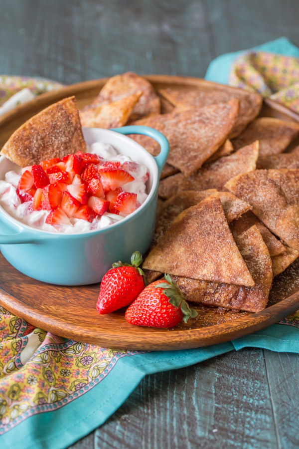 Gebackene Zimtchips auf einem Holzteller mit einer Schüssel cremigem Erdbeerdip und ein paar ganzen Erdbeeren. 