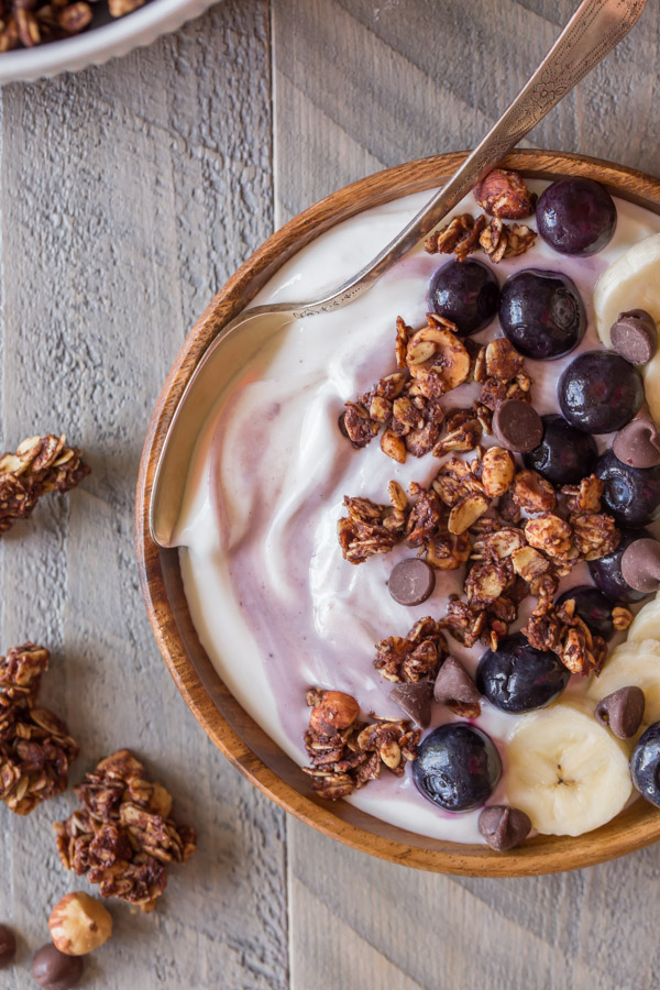 Chocolate Hazelnut Granola Yogurt Bowl with a spoon in it and some granola pieces around the bowl. 