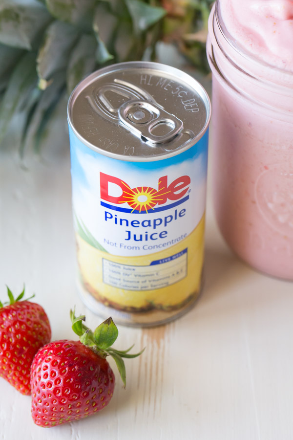 A can of Dole Pineapple Juice, next to a glass jar of Dole Pineapple Strawberry Cream Slush and some whole strawberries.  
