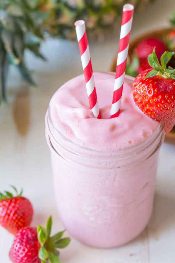 Dole Pineapple Strawberry Cream Slush in a glass jar, with two straws and a strawberry on the rim of the jar. 