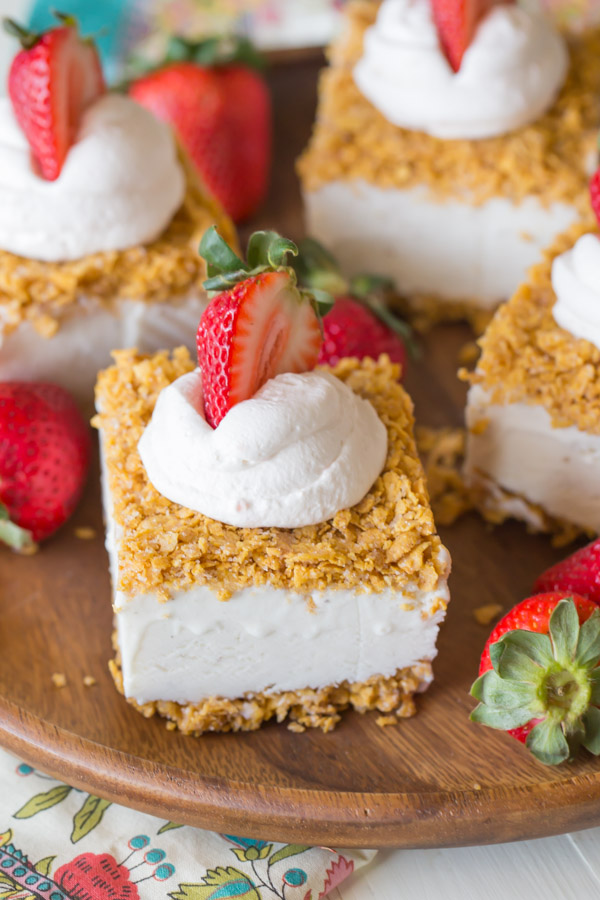 Fried Ice Cream Bars topped with whipped cream and a sliced strawberry, arranged on a wood plate with whole strawberries.  
