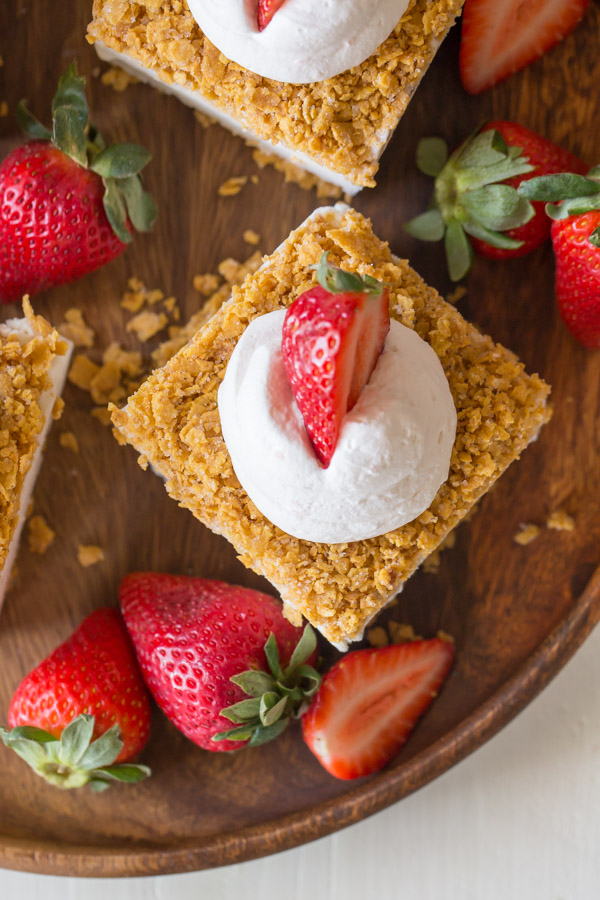 Fried Ice Cream Bars topped with whipped cream and a sliced strawberry, arranged on a wood plate with whole strawberries.  