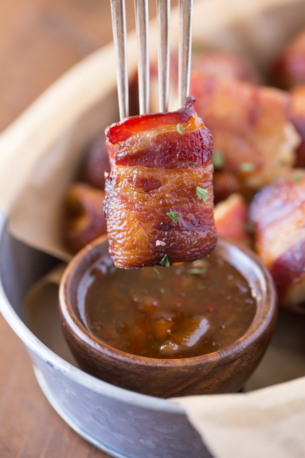A Bacon Wrapped Chicken Bite on a fork about to be dipped into a small cup of Apricot Pepper Dipping Sauce.