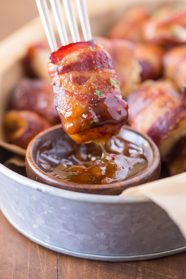 A Bacon Wrapped Chicken Bite on a fork that has been dipped into a small cup of Apricot Pepper Dipping Sauce.