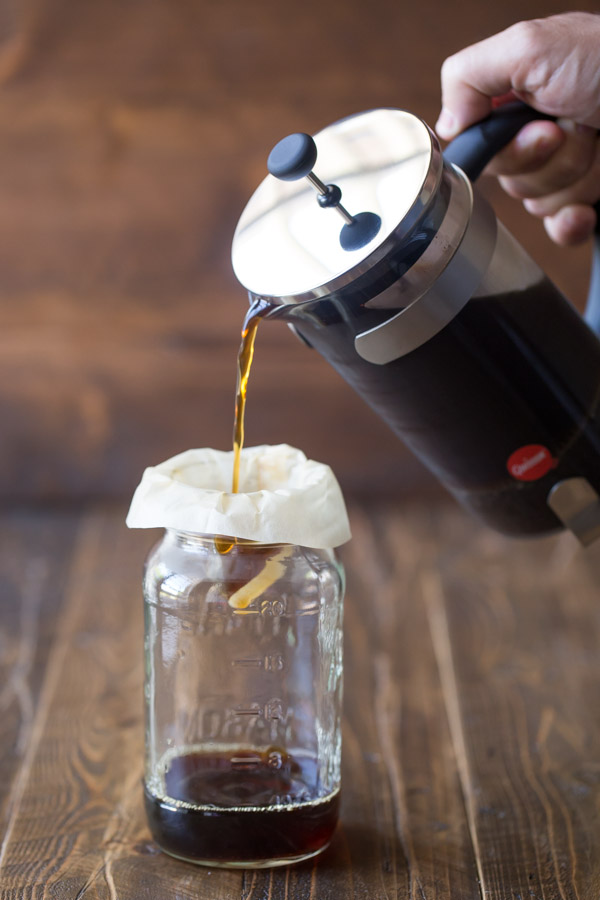Coffee from a French press being poured through a coffee filter and into a jar.