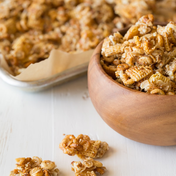 Healthier Coconut Almond Chex Mix in a wood bowl with more Chex mix on a parchment paper lined baking sheet in the background.  