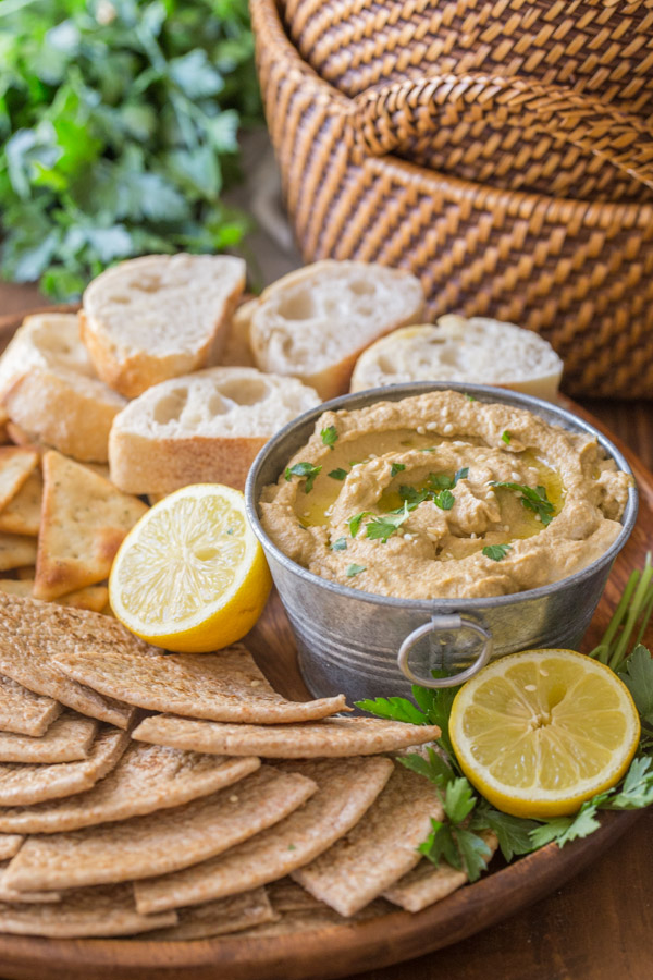 Roasted Eggplant Dip in a galvanized mini bucket for serving, on a wood tray with pita wedges, French bread slices, crackers and a lemon sliced in half.
