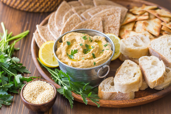 Roasted Eggplant Dip in a galvanized mini bucket for serving, on a wood tray with pita wedges, French bread slices, crackers and a lemon sliced in half, with some toasted sesame seeds and fresh parsley next to the tray.  