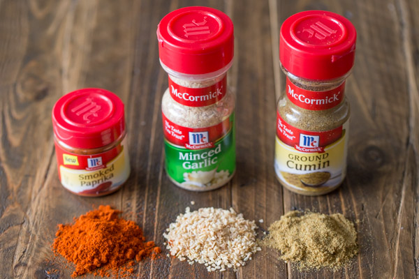 A McCormick Smoked Paprika container, a McCormick Minced Garlic container and a McCormick Ground Cumin container lined up with a pile of the spice in front of each container.  
