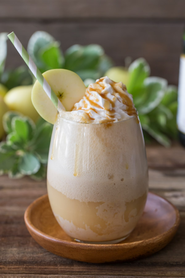 Caramel Apple Float topped with whipped cream and caramel, with a straw and an apple slice on the rim of the glass. 