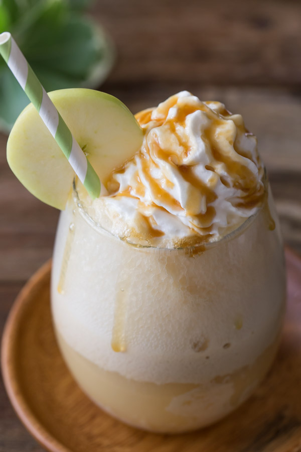 Caramel Apple Float topped with whipped cream and caramel, with a straw and an apple slice on the rim of the glass. 
