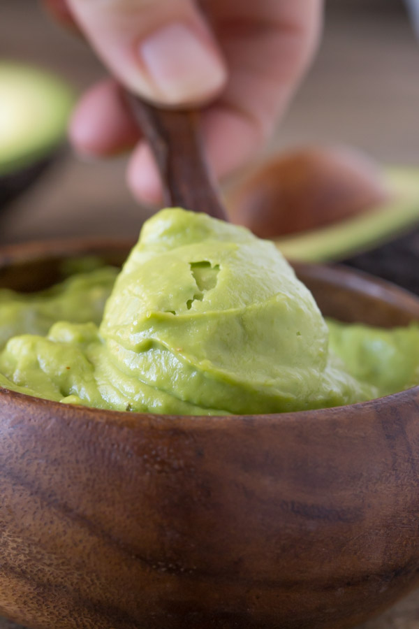 Whipped Avocado Cream in a small wood bowl, with a small wood spoon dipped into it.  