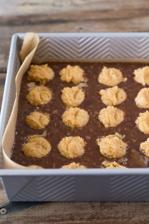 Homemade brownie batter studded with globs of peanut butter cookie dough in a parchment paper lined baking pan. 