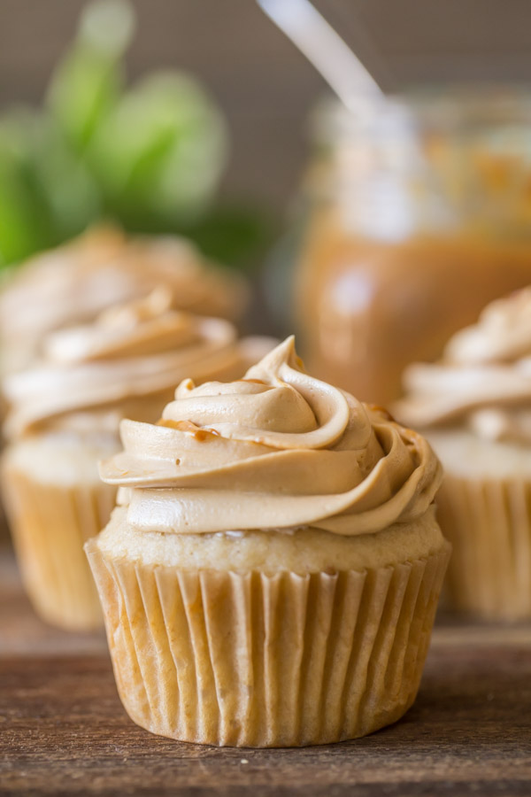Apple Cupcake With Dulce De Leche Buttercream, with more cupcakes in the background along with a mason jar of dulce de leche. 