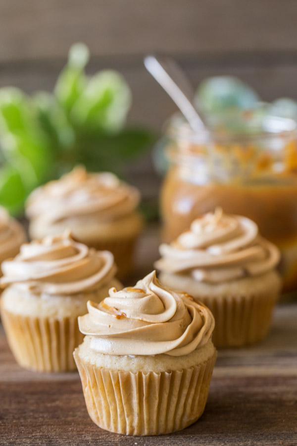 Apple Cupcake With Dulce De Leche Buttercream, with more cupcakes in the background along with a mason jar of dulce de leche. 