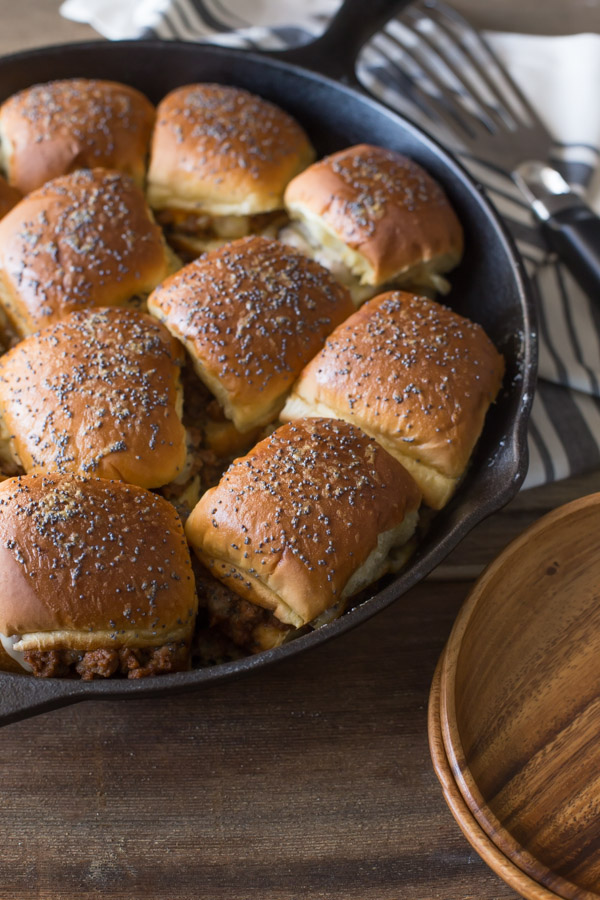 Party Bun Style Sloppy Joes in a cast iron skillet, with a serving spatula and some wood plates next to the skillet.  