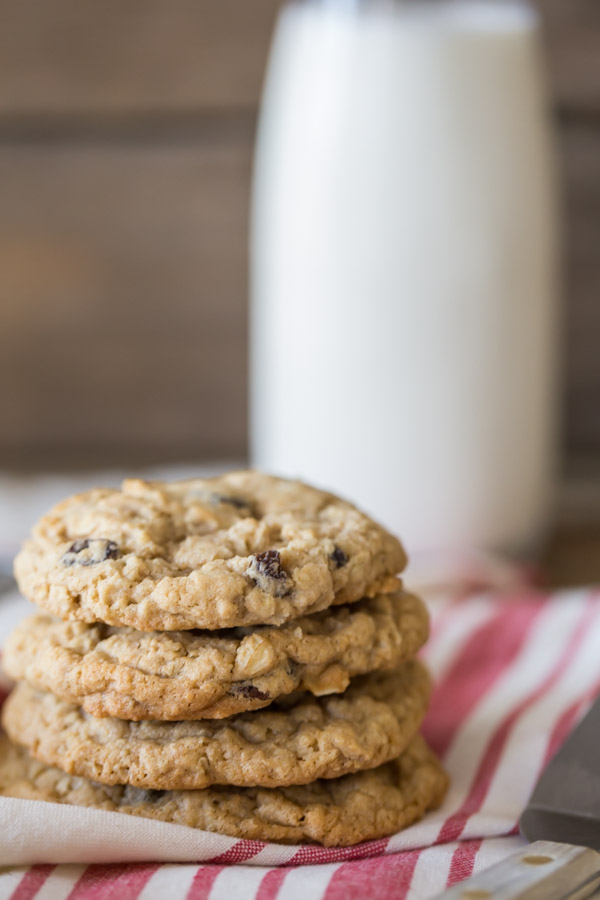 Pumpkin Pie Spice Oatmeal Raisin Cookies stacked in a pile of four, with a glass of milk in the background.  