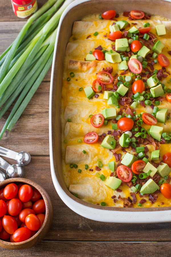 Breakfast Enchilada Bake with toppings in a baking dish, with grape tomatoes, measuring spoons, green onions, and a spice container next to the baking dish. 