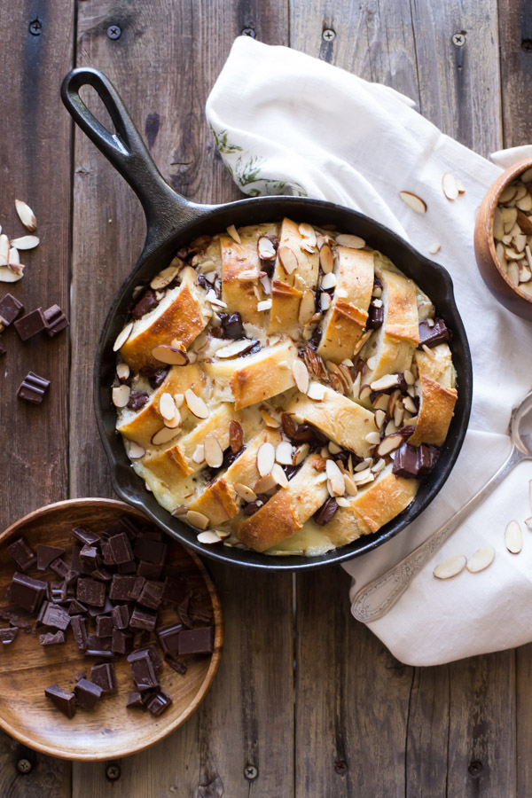 Chocolate Almond Bread Pudding in a cast iron skillet, with chopped chocolate and slivered almonds next to it. 