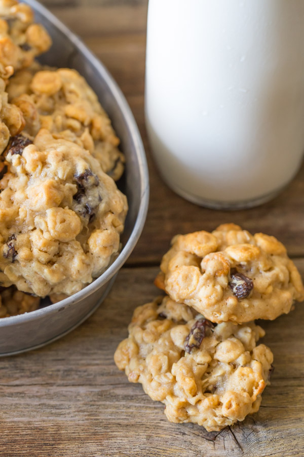Two Healthy Breakfast Cookies sitting next to a galvanized metal bowl full of cookies and a glass of milk. 