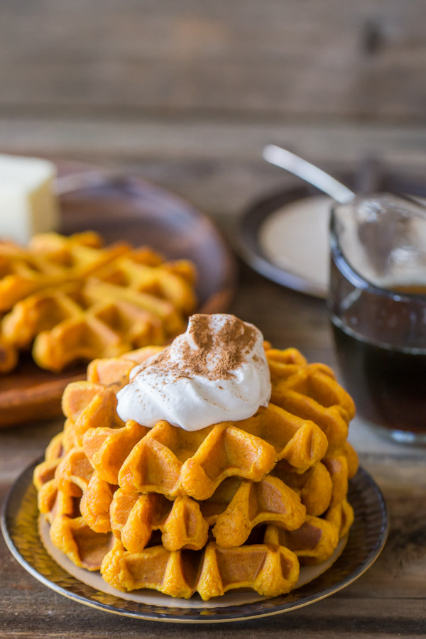 Pumpkin Spice Waffles stacked on a plate, topped with whipped cream and cinnamon.  