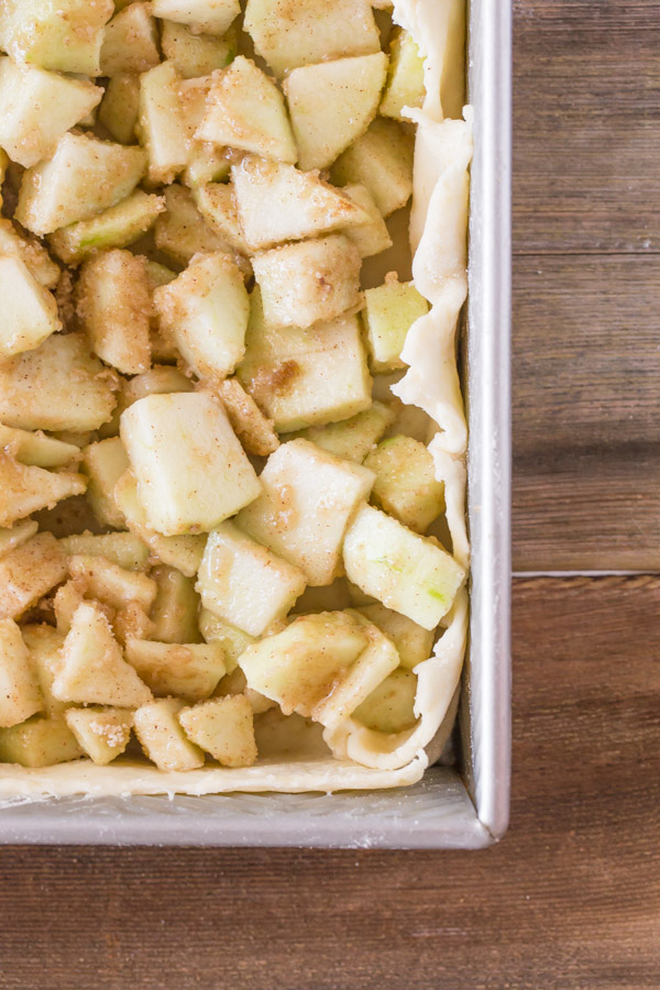 A baking pan with the bottom pie dough and apple mixture in it for the Iced Apple Pie Bars.