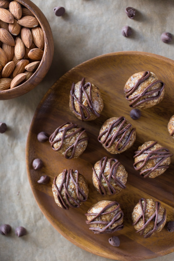 No Bake Energy Bites on a wood plate, drizzled with melted chocolate, sitting next to a bowl of almonds.  