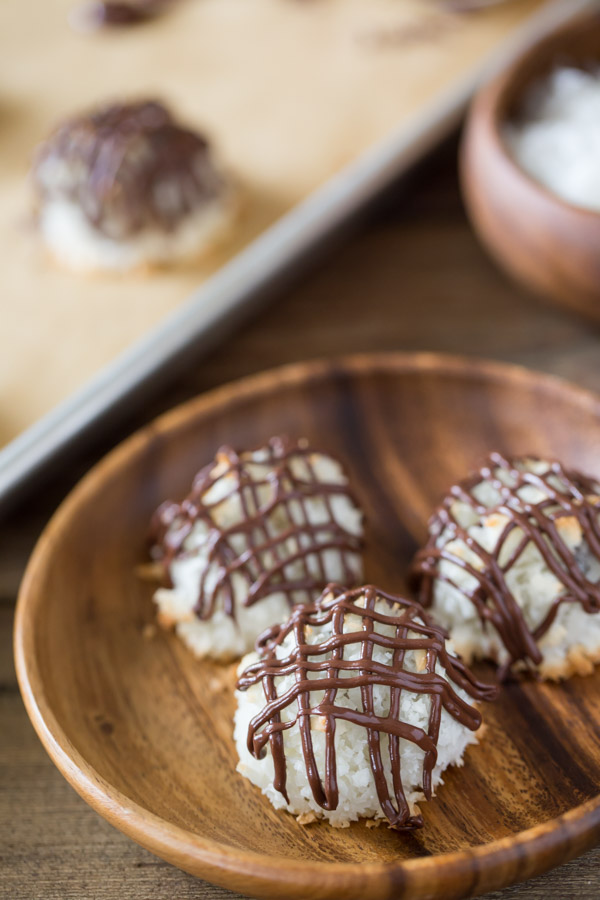 Three Stuffed Chocolate Almond Macaroons that have been drizzled with chocolate, sitting on a wood plate.