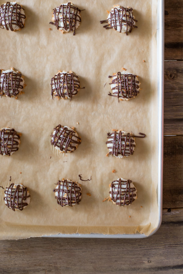 Stuffed Chocolate Almond Macaroons that have been drizzled with chocolate, sitting on a parchment paper lined baking sheet.