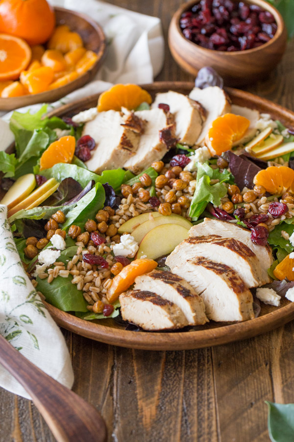 Turkey Farro Salad With Candied Chickpeas on a wood serving plate, with a wood plate of clementines and a wood bowl of dried cranberries in the background.  