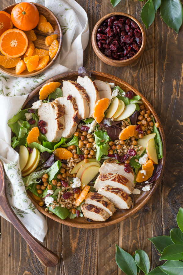Turkey Farro Salad With Candied Chickpeas on a wood serving plate, with a wood plate of clementines and a wood bowl of dried cranberries next to it.  