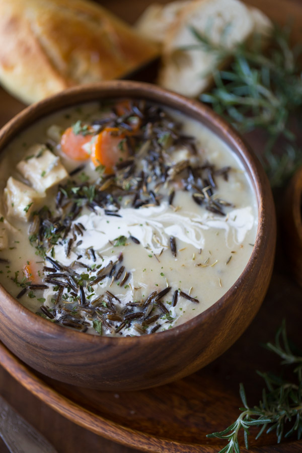 Creamy Chicken and Wild Rice Soup in a wood bowl, sitting on a wood plate along with some bread.  