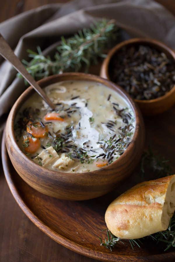 Creamy Chicken and Wild Rice Soup in a wood bowl, sitting on a wood plate along with a small wood bowl of wild rice and a piece of bread.  