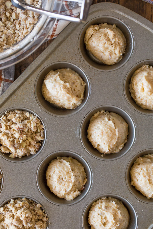 A muffin pan filled with the Banana Muffin batter, and some of the batter has been topped with the Almond Oat Streusel Topping.  